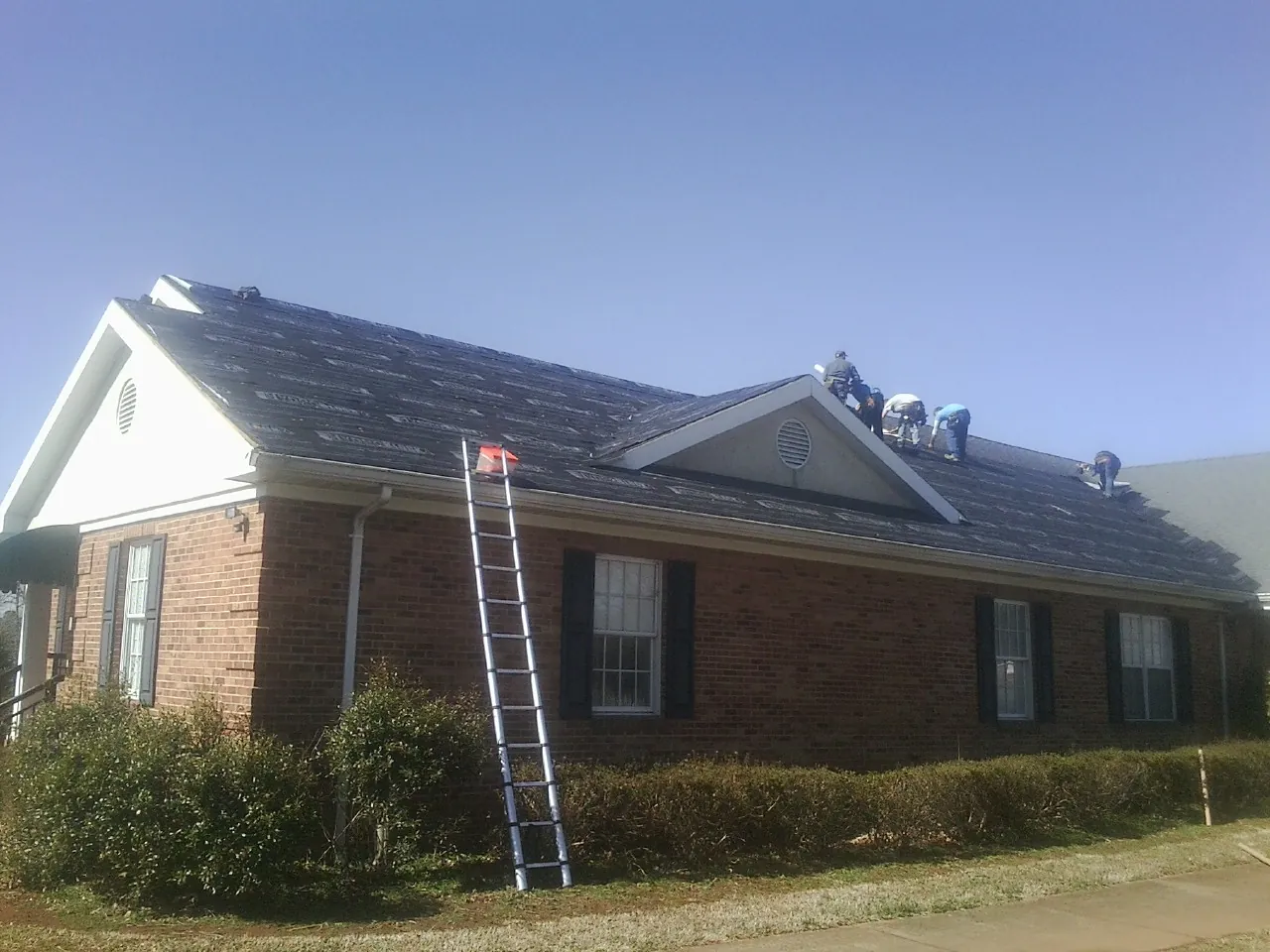 Crew tearing shingles off a brick ranch roof with a ladder set — Emergency Roof Repair work by our crew in Pamplico