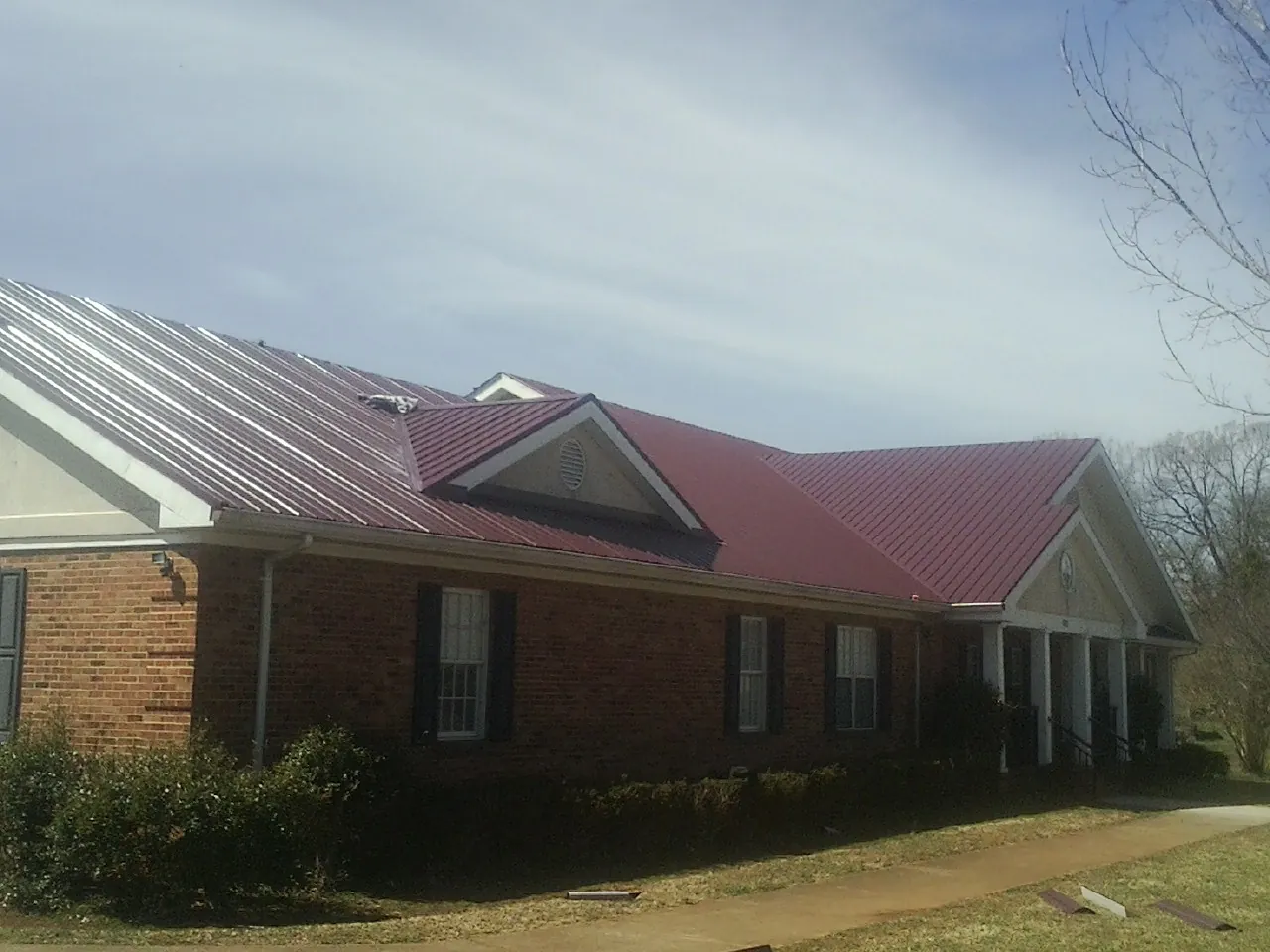 Red metal roof with gabled entries on a long brick building, from a Hail Damage Roof Repair job in Pamplico