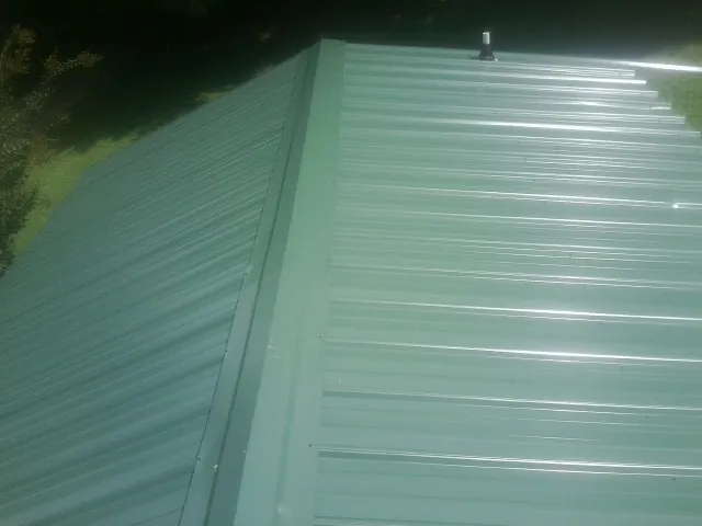 New green metal panels meeting at the ridge of a roof — Flat Roof Repair work by our crew in Pamplico
