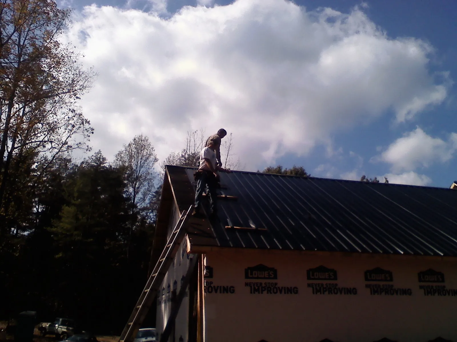 Roofer fastening dark metal panels high against a cloudy sky, from a Roof Inspection job in Pamplico