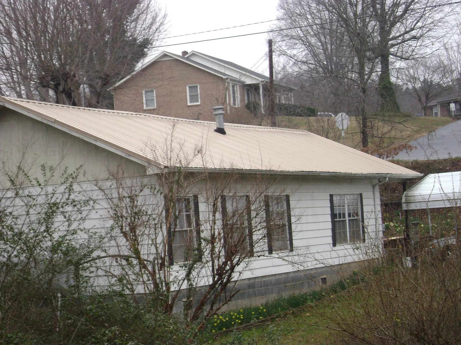 Tan metal roof on a white sided house set into a hillside — Commercial Roofing by Roofing Brothers in Pamplico